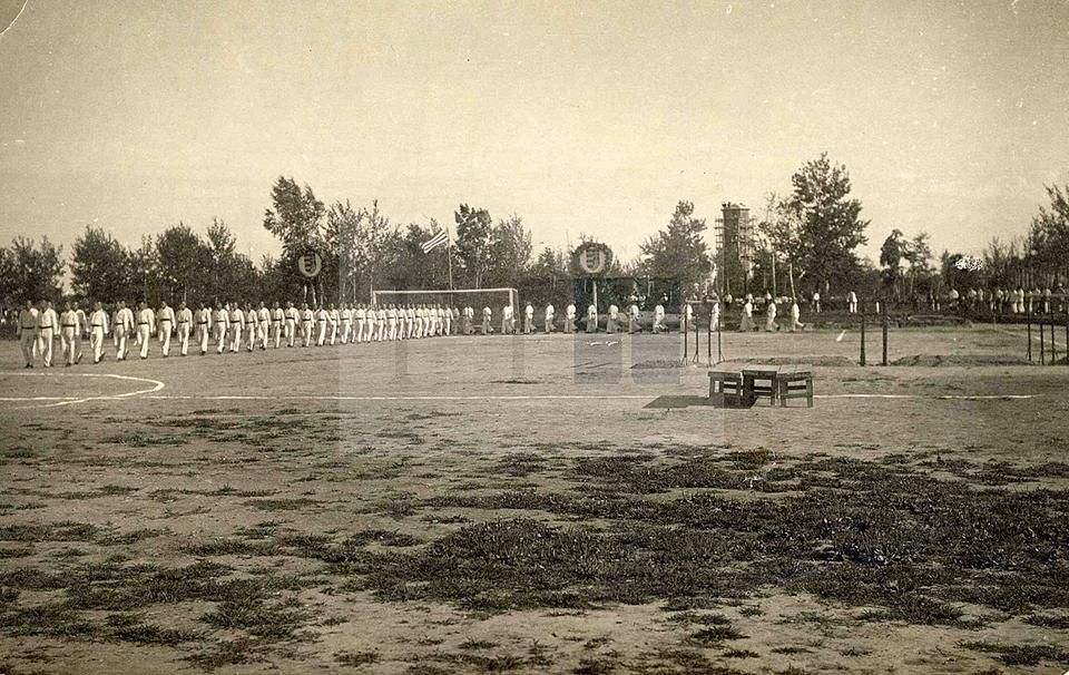 Ünnepi felvonulás Szent István tiszteletére a habarovszki tábor kopott futballpályáján 1918-ban, a kapu fölött jobbra és balra növénykoszorúval díszített magyar címer látszik